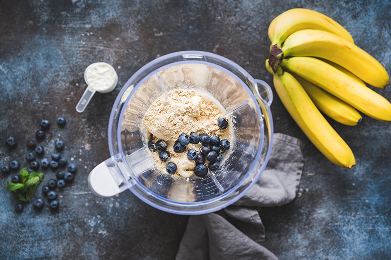 Aerial view of a blender filled with protein powder, blueberries, and bananas